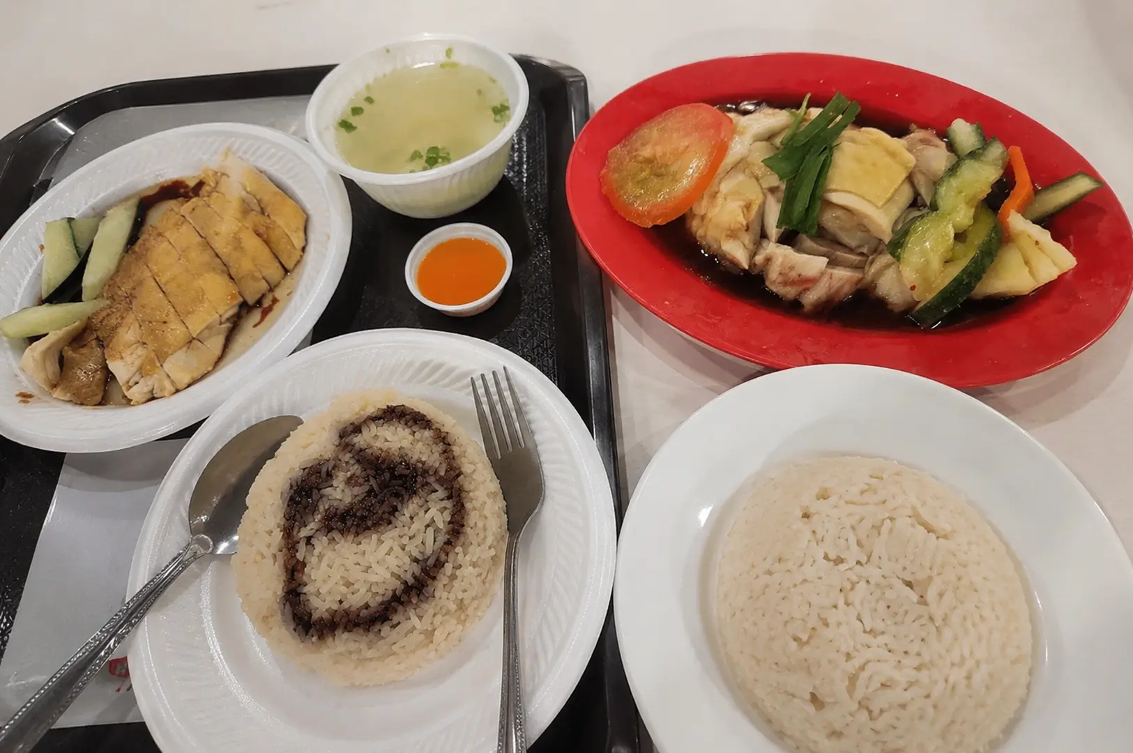 Food tray with two servings of Hainanese chicken rice, soup, and chili sauce