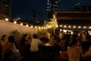 Outdoor seating area at a hidden Singapore bar filled with guests enjoying drinks beneath warm string lights and the city skyline