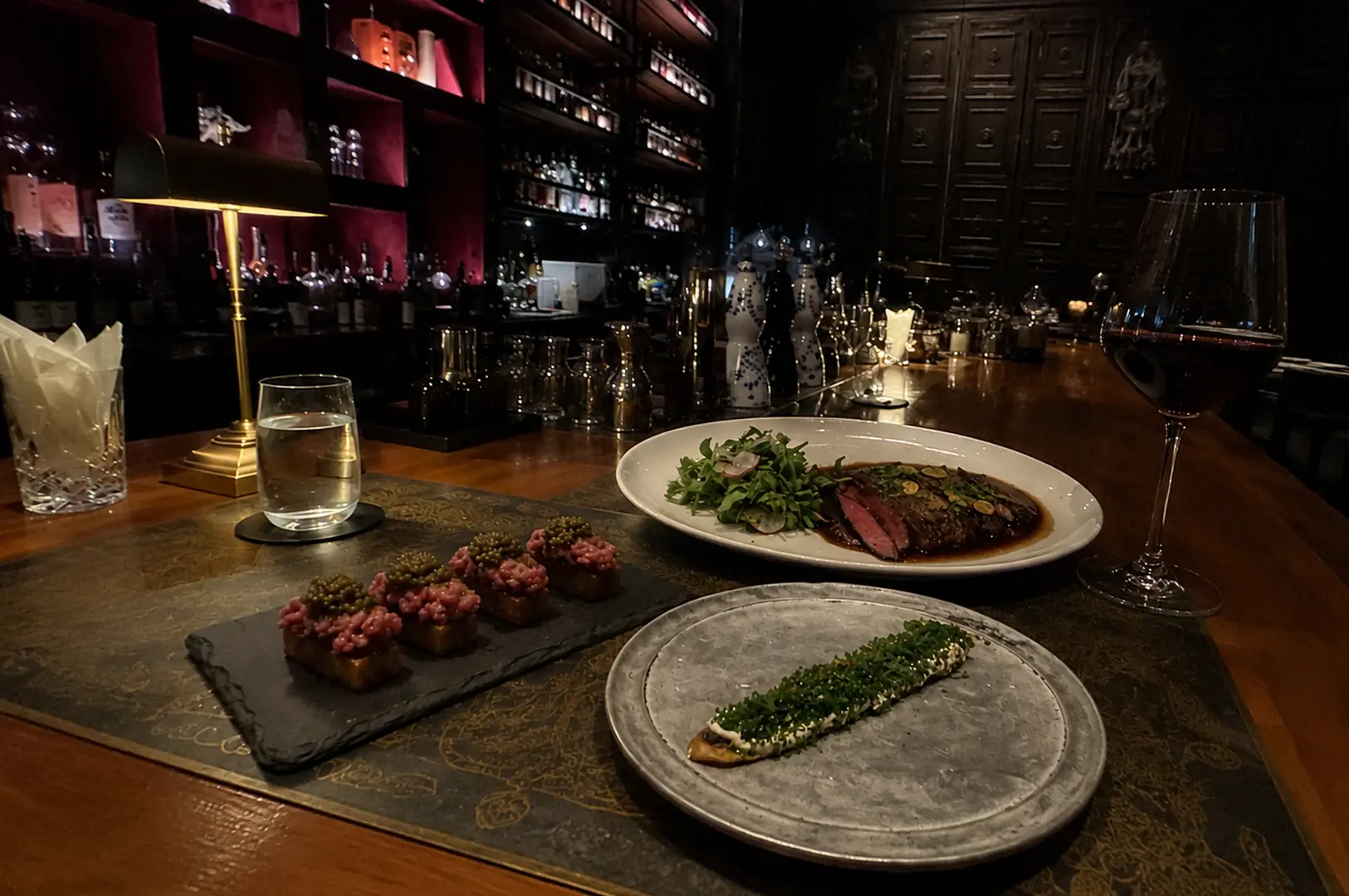 Sophisticated table setting featuring steak, caviar appetizers, and red wine in a dimly lit, moody restaurant interior
