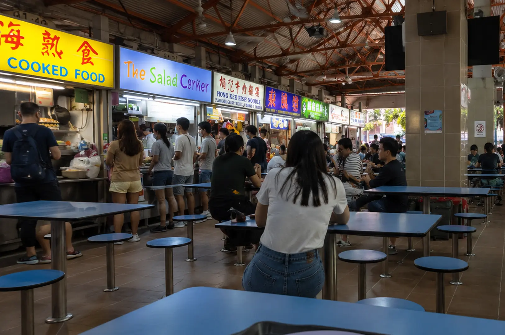 Diners queue at hawker stalls like The Salad Corner and Hong Kee Fish Noodle in a busy cooked food center