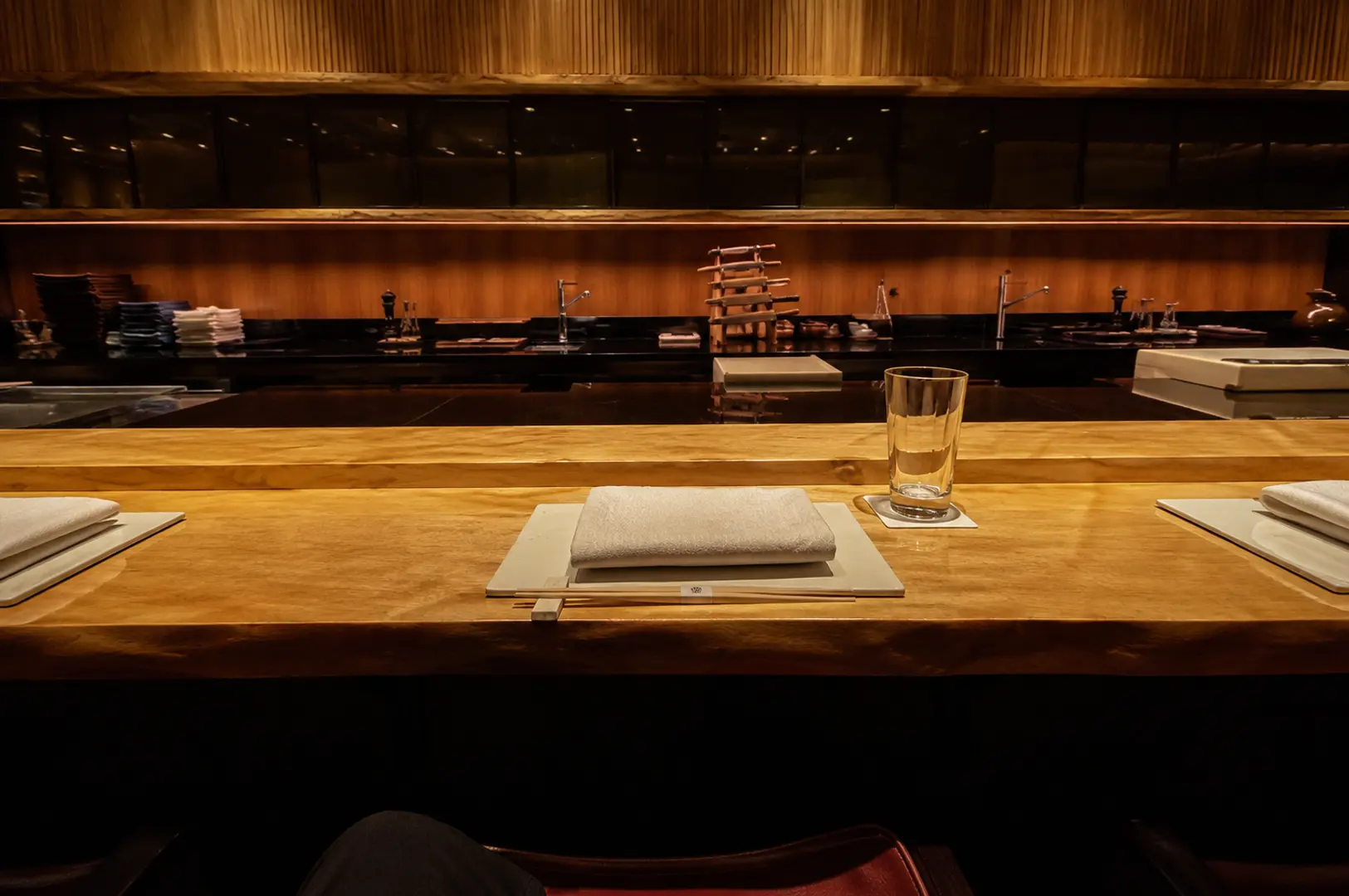 Wooden omakase counter set with folded towels, chopsticks, and plates for an intimate dining experience