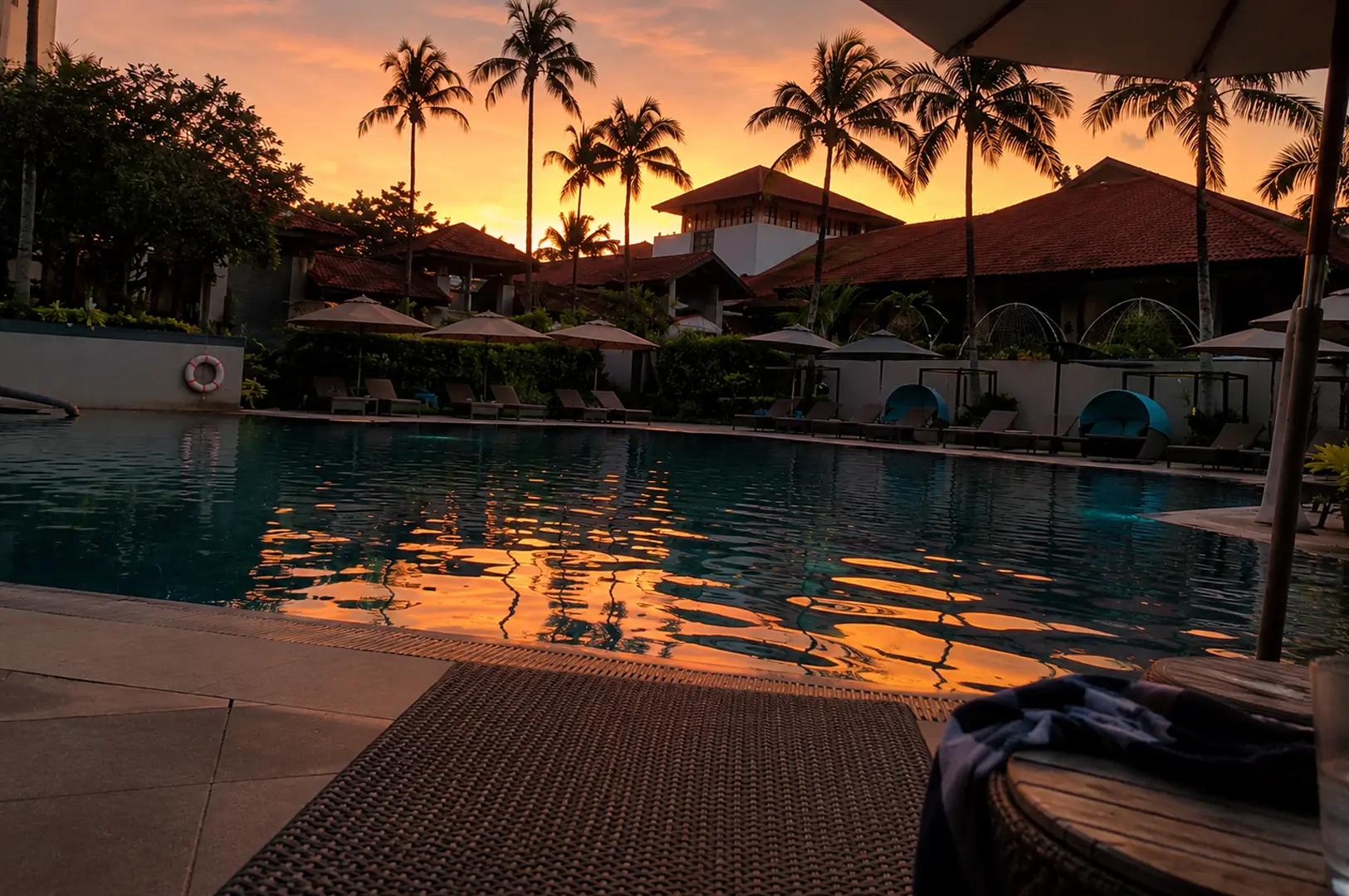 Resort swimming pool at sunset with palm trees and lounge chairs, suitable for an exclusive outdoor private event