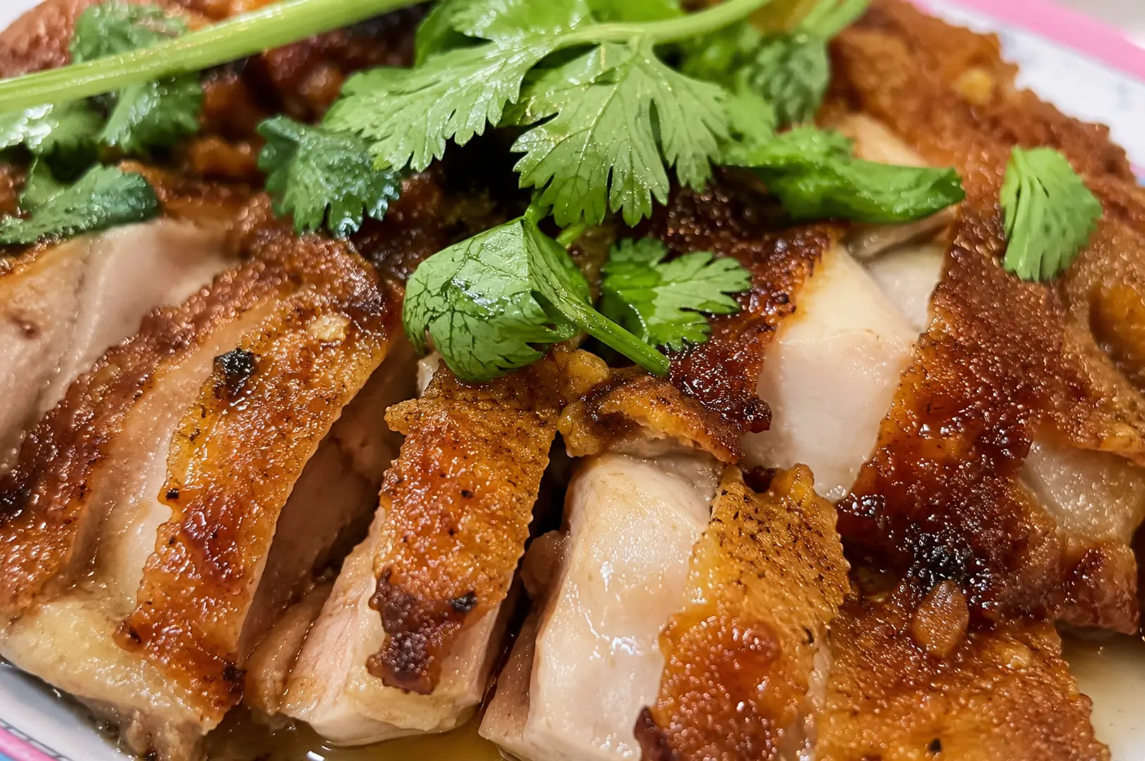 Close-up of crispy roasted chicken slices with fresh cilantro garnish