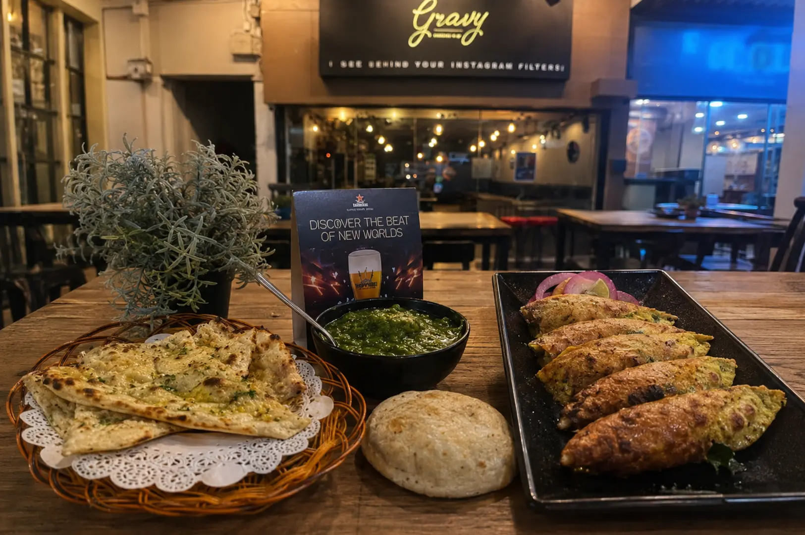Indian cuisine spread with garlic naan, seekh kebabs, and green chutney displayed at Gravy restaurant with illuminated signage visible in the background
