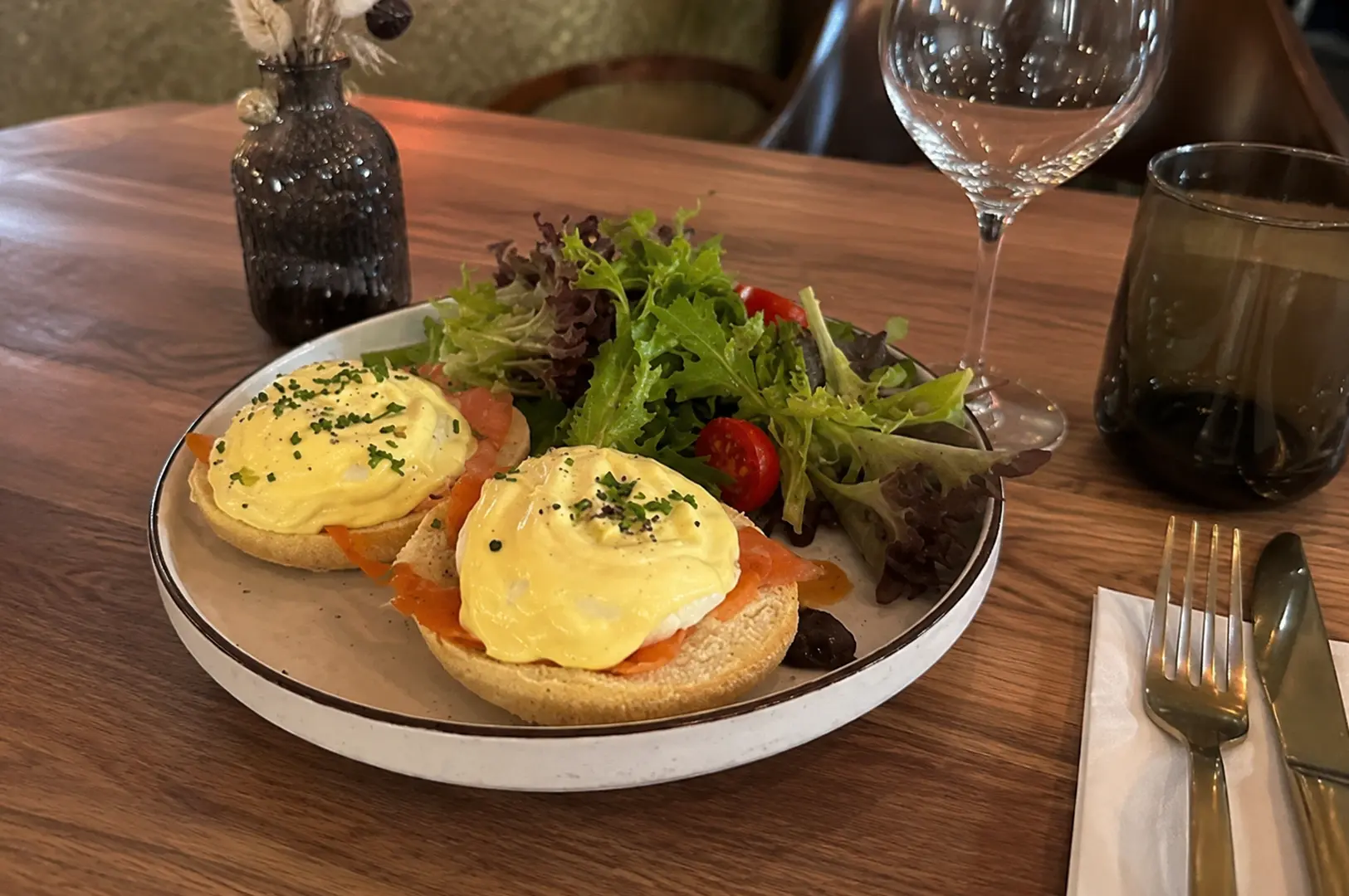 Smoked salmon eggs benedict with hollandaise sauce and mixed greens served with wine at an upscale brunch restaurant.