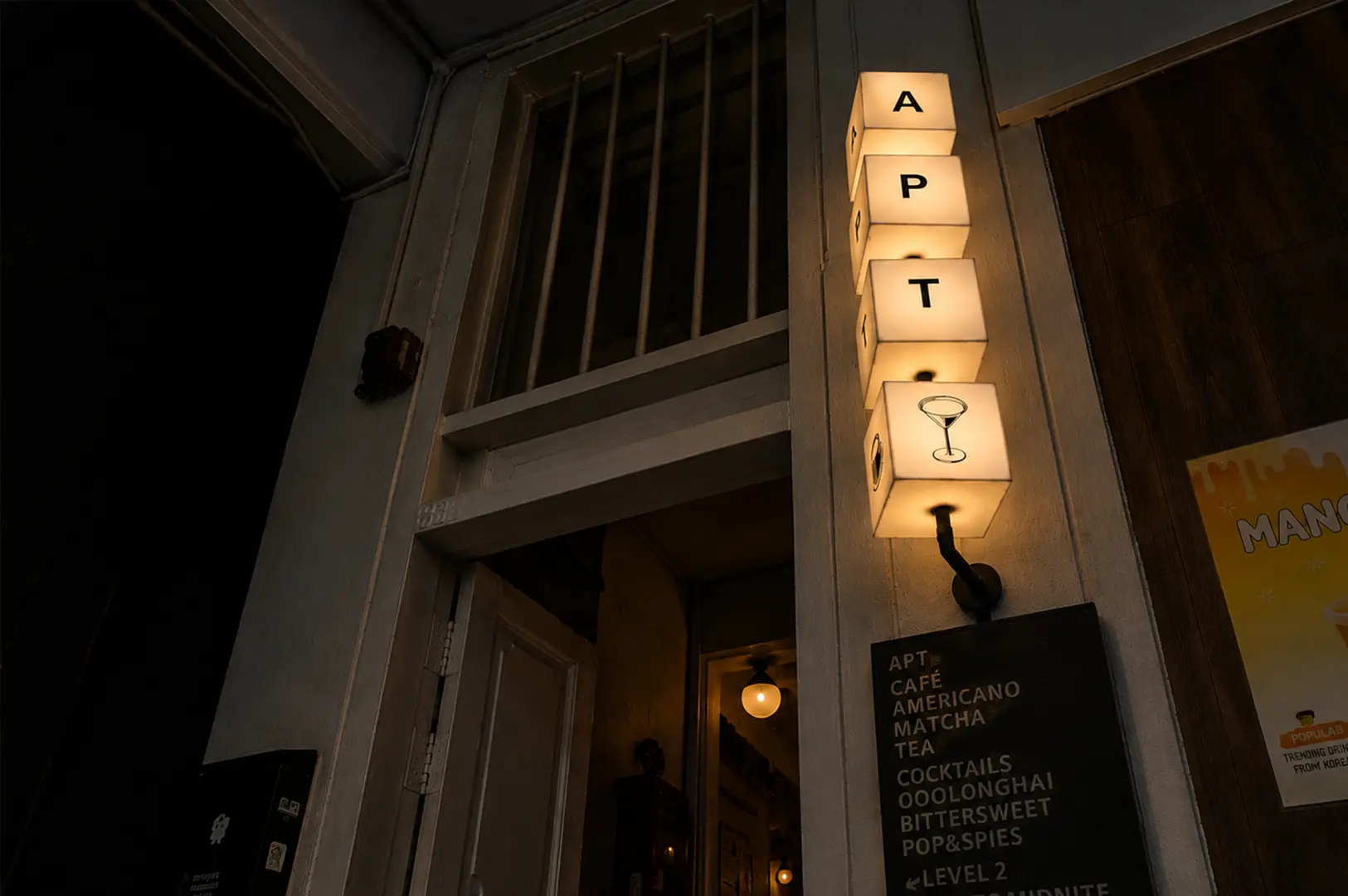 Nighttime view of APT Tanjong Pagar's understated entrance with its glowing vertical sign, giving the hidden cocktail café a cozy and inviting speakeasy feel.