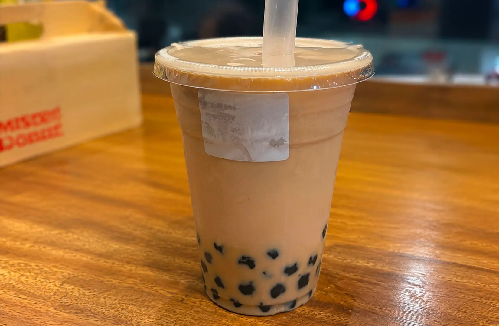 A plastic cup of milk tea with boba pearls and a wide straw on a wooden table