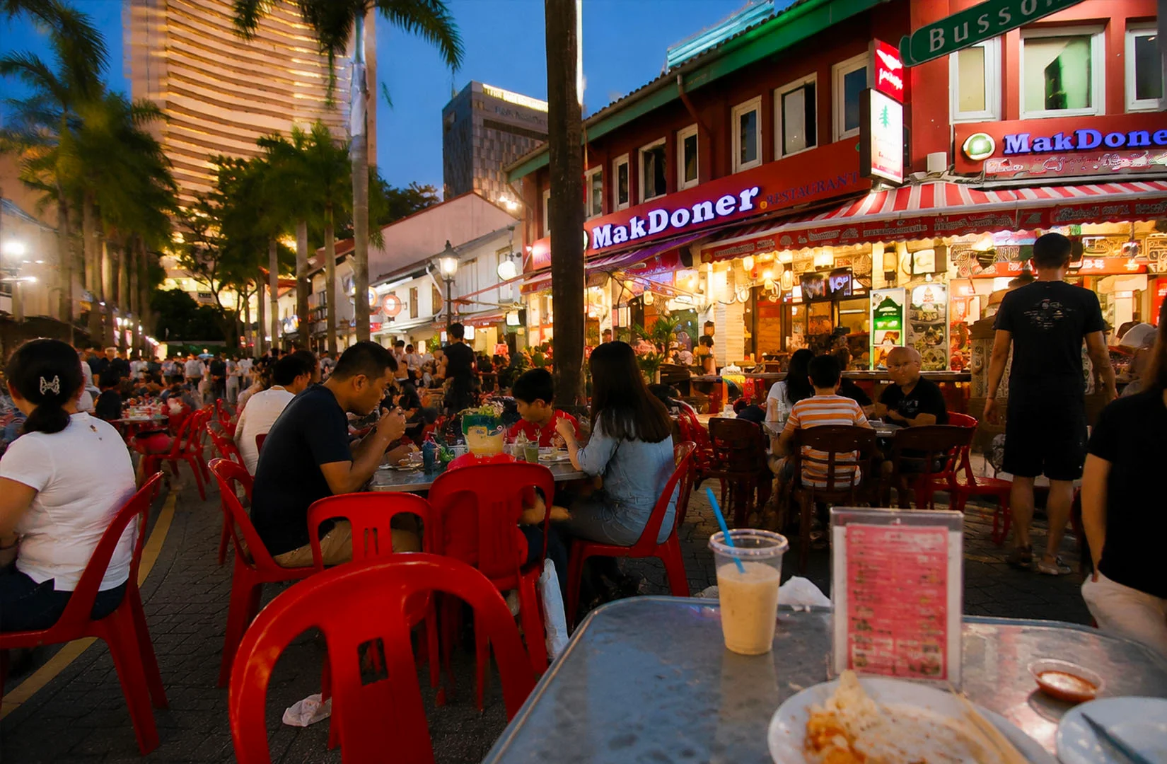 A busy Singapore outdoor dining street with restaurants and diners enjoying different cuisines, highlighting the city’s multicultural food environment.