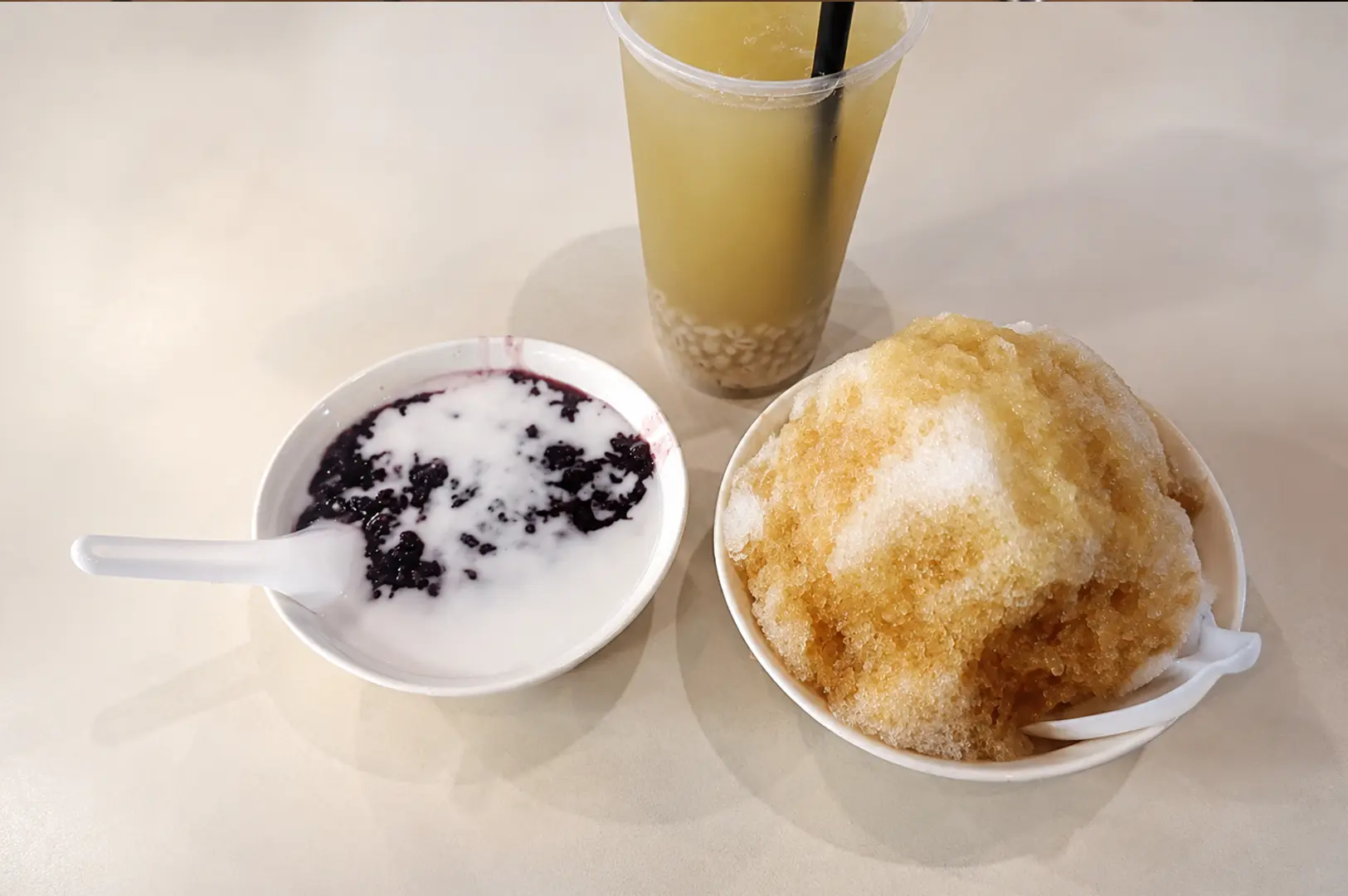 Traditional Singapore desserts featuring black glutinous rice with coconut milk, shaved ice dessert with syrup, and a cup of barley drink with pearls