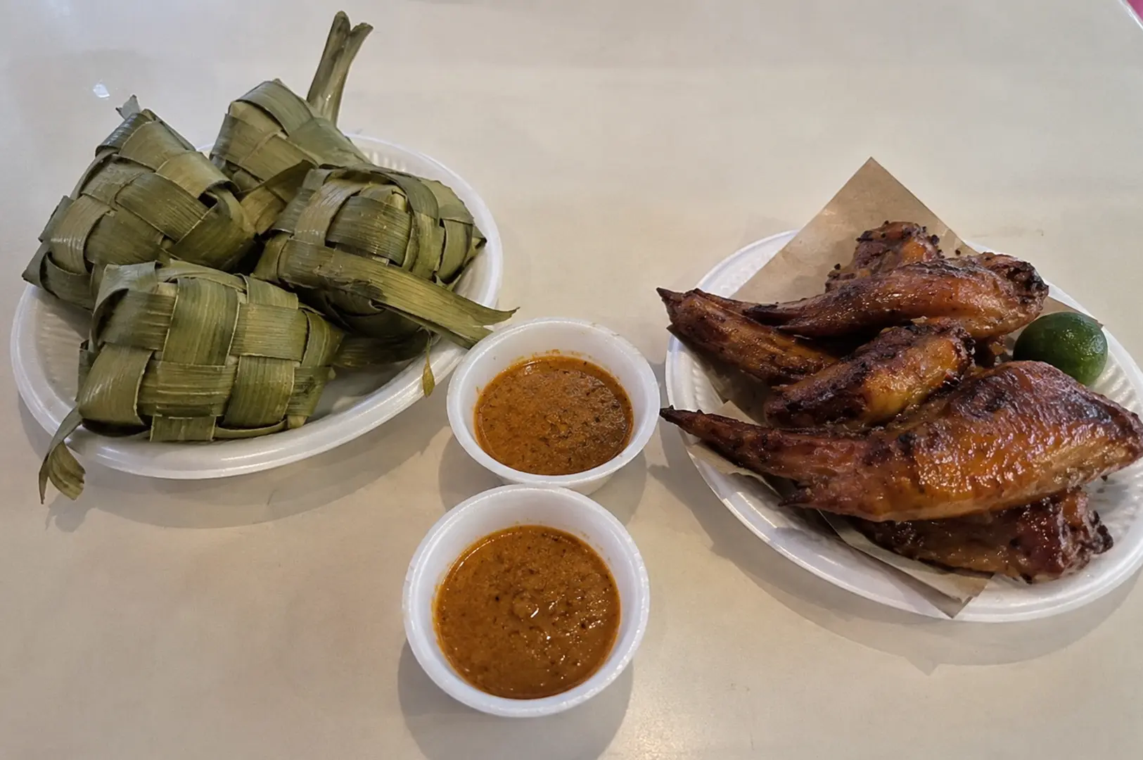 Woven ketupat rice cakes served with grilled BBQ chicken wings and two bowls of rich peanut dipping sauce