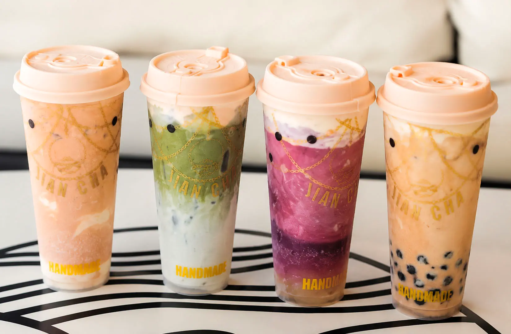 Four colorful handmade bubble tea drinks from Jian Cha in peach, green, purple, and classic flavors lined up in a row