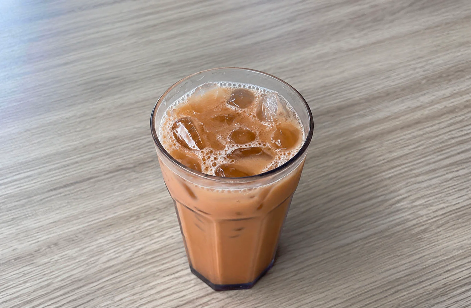 A glass of iced kopi on a wooden table in a Singapore setting.