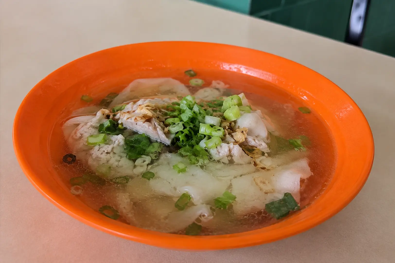 A bowl of clear fish soup with cabbage and spring onions served in a classic orange hawker bowl