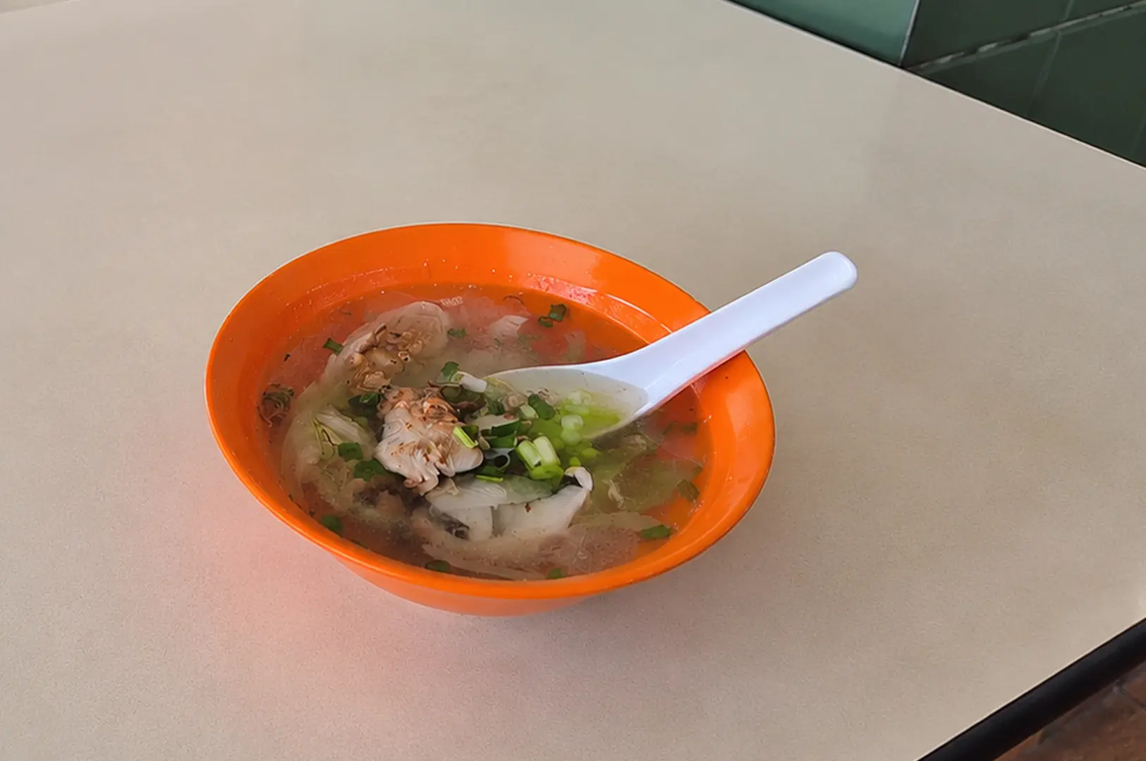 A bowl of clear fish soup with cabbage and spring onions served in a classic orange hawker bowl