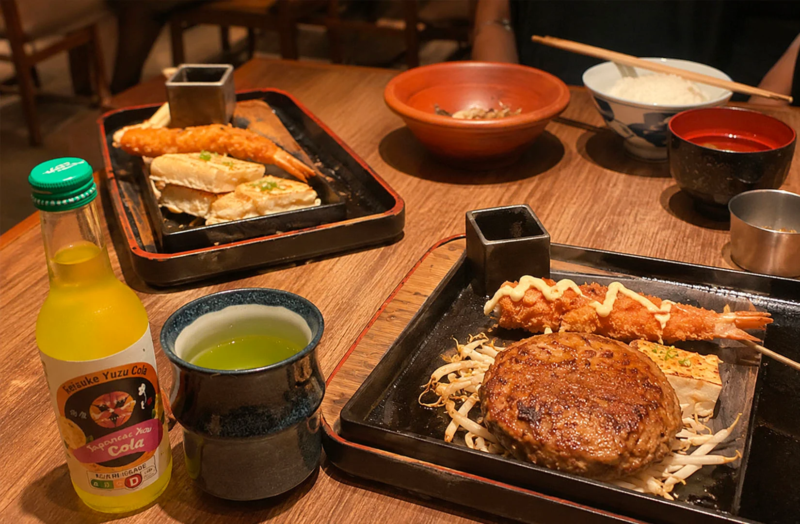 Japanese hamburg steak meal served on hot plates with shrimp, rice, soup, and drinks.
