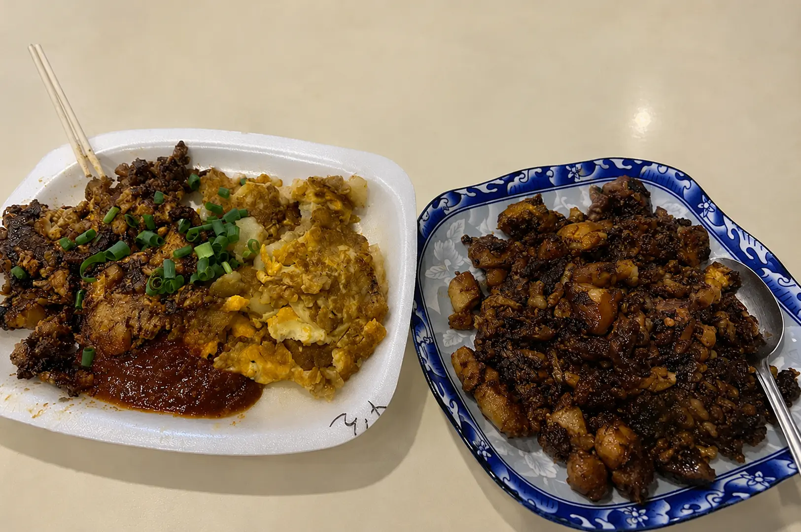Oyster omelette with fried egg and spring onions served with chili sauce, alongside a blue-patterned plate of black carrot cake (chye tow kway) stir-fried in dark soy sauce
