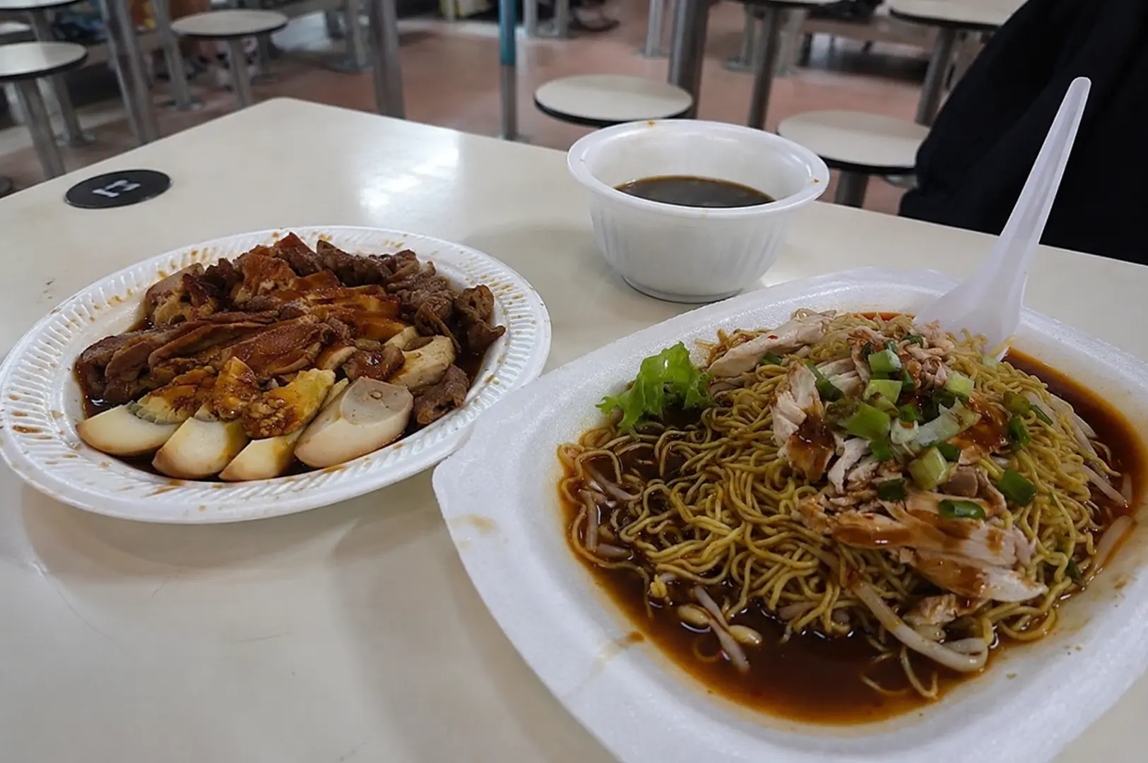 Braised duck with hard-boiled eggs in dark soy sauce paired with a bowl of chicken noodles topped with shredded meat, lettuce, and spring onions