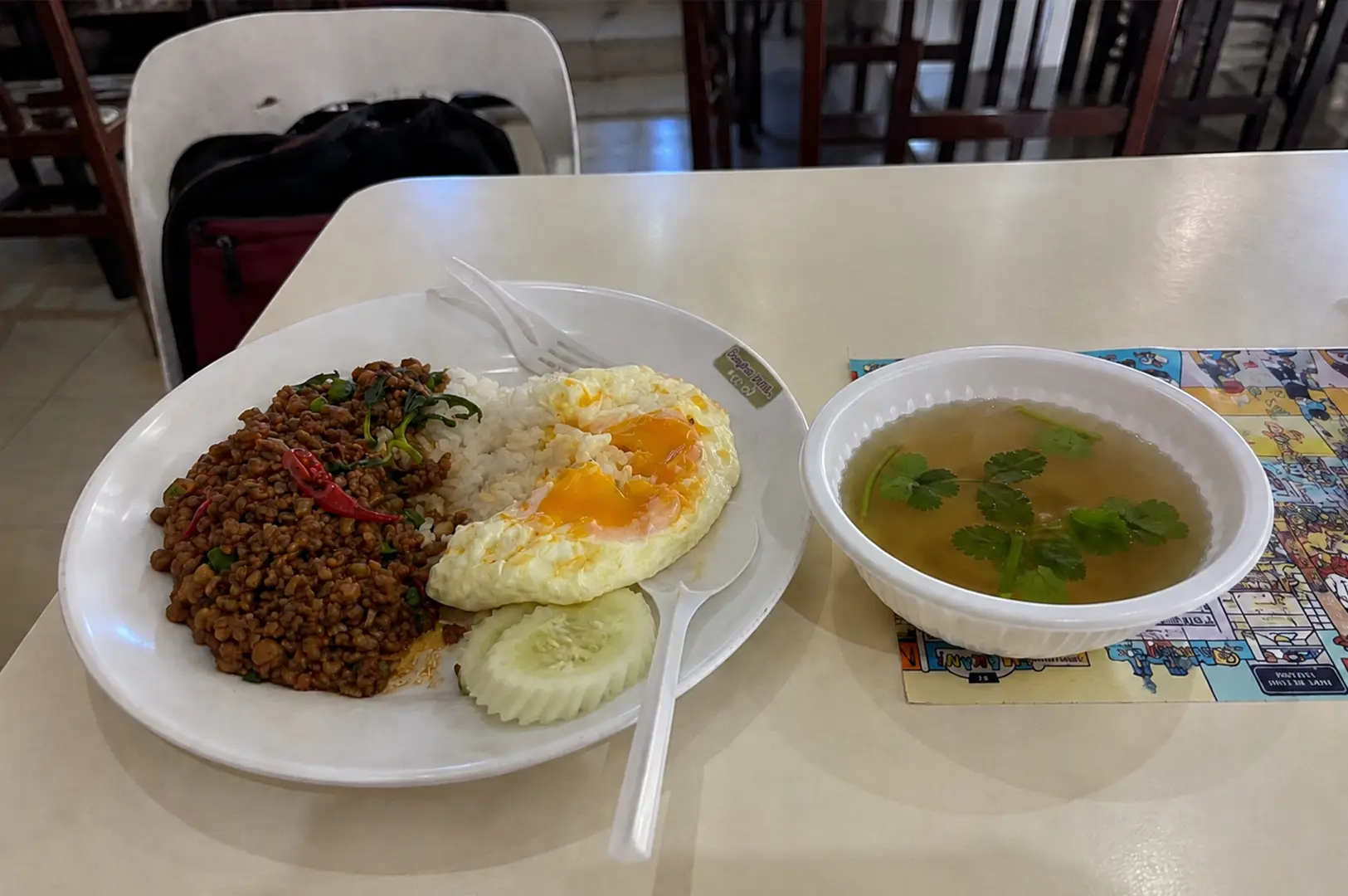 Plate of minced meat rice with two fried eggs served alongside a clear soup.