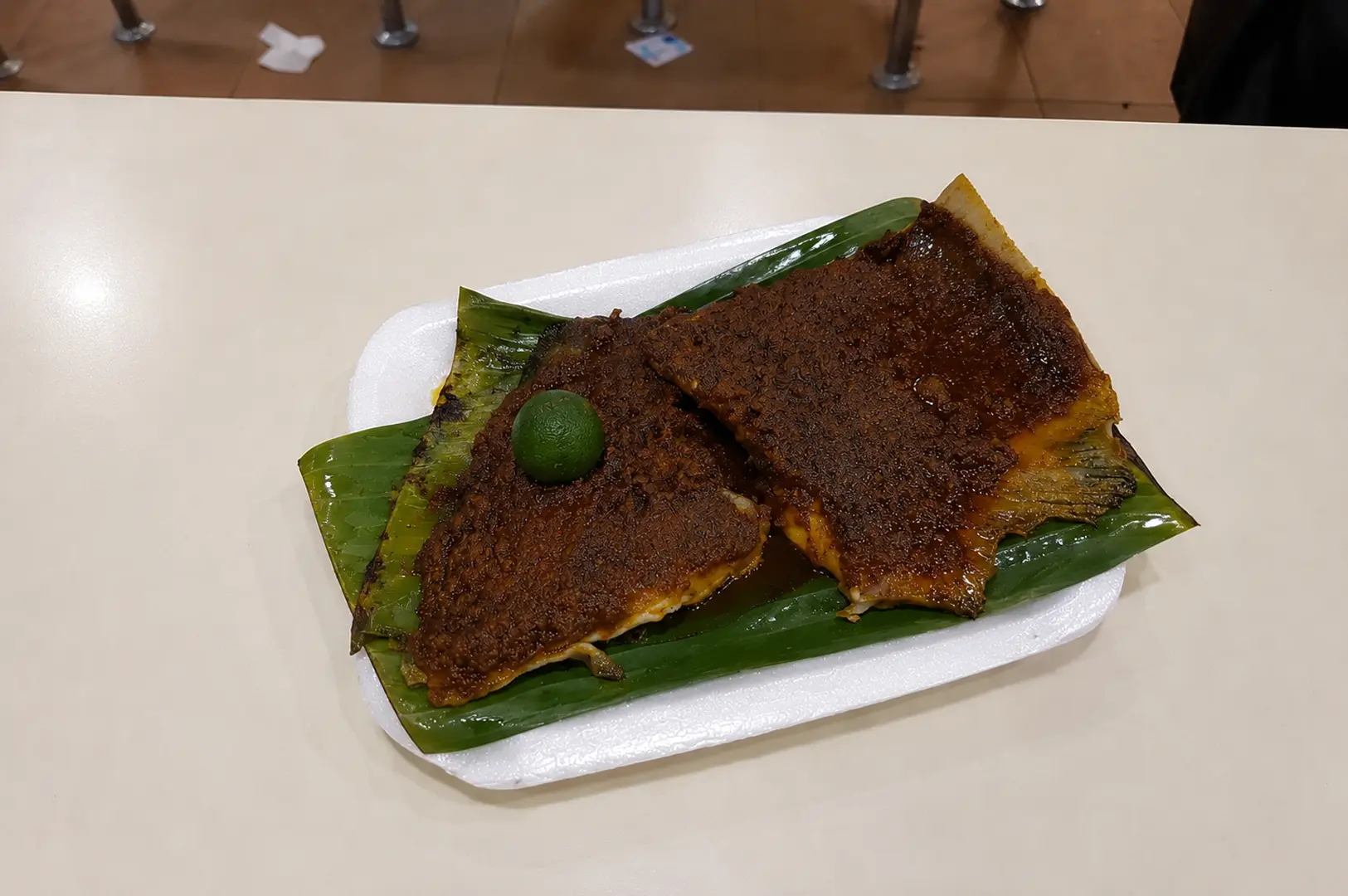 BBQ sambal stingray served on a banana leaf with a calamansi lime in a white disposable plate