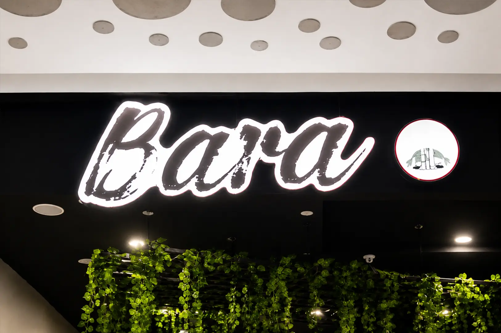 Bara Food Tanjong Pagar illuminated restaurant sign above a lush green plant display.