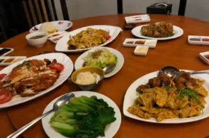Singaporean Chinese meal with roasted chicken, braised tofu, mushrooms, leafy greens, meatballs, and rice served on a round table.