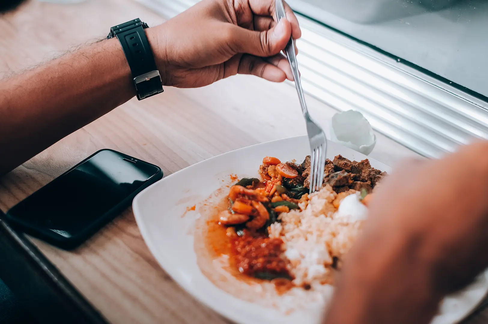 Person enjoying a solo meal of rice and local dishes at a casual dining table in Singapore.