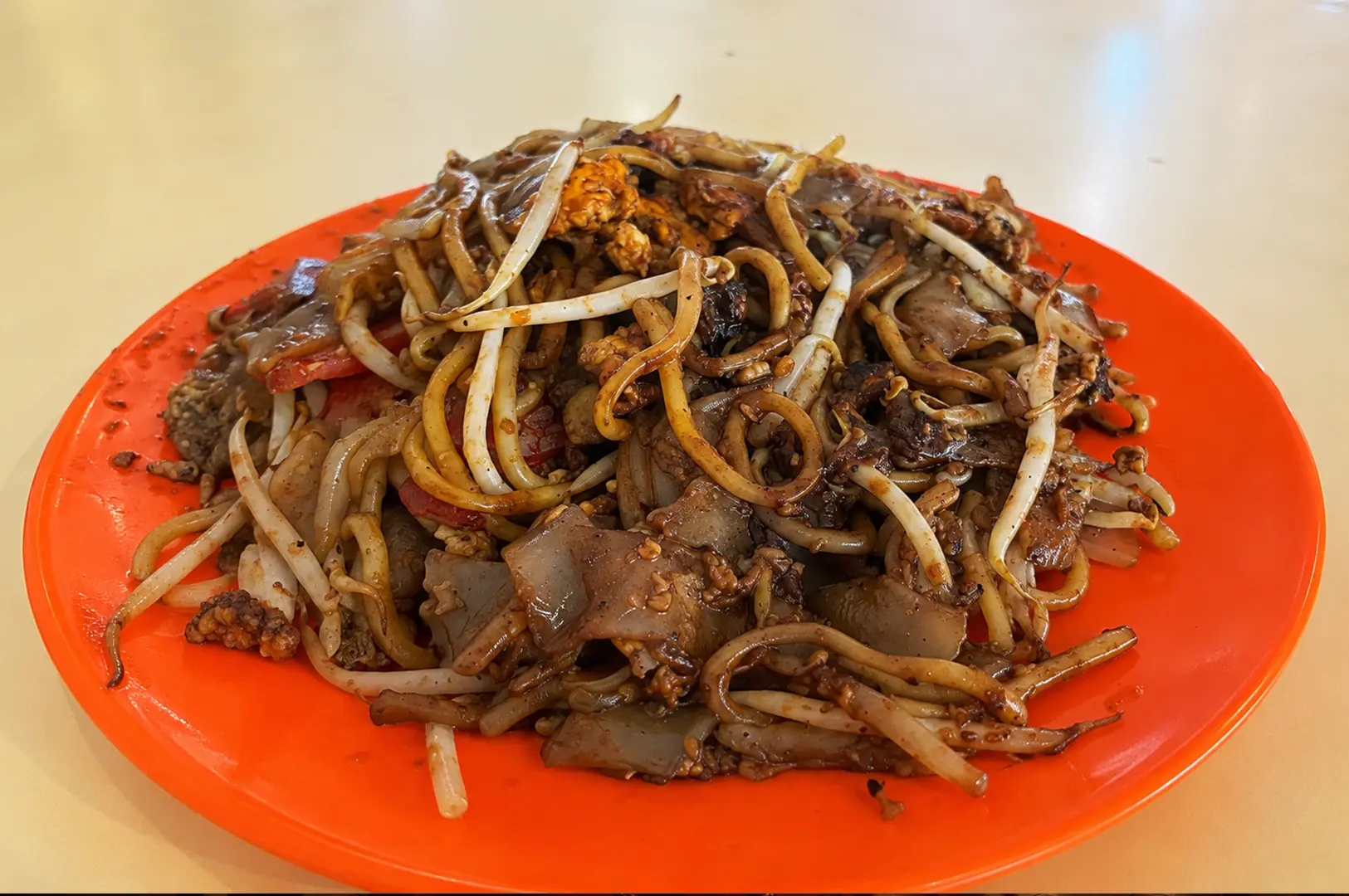 Stir-fried kway teow with bean sprouts and mixed ingredients on a bright orange plate.