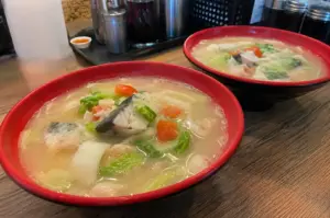Two bowls of traditional Singapore fish soup served on a wooden table in a casual side-angle phone shot.