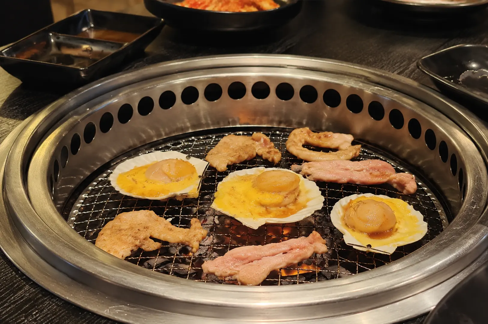 Assorted meats and scallops grilling over charcoal at a Korean barbecue restaurant.