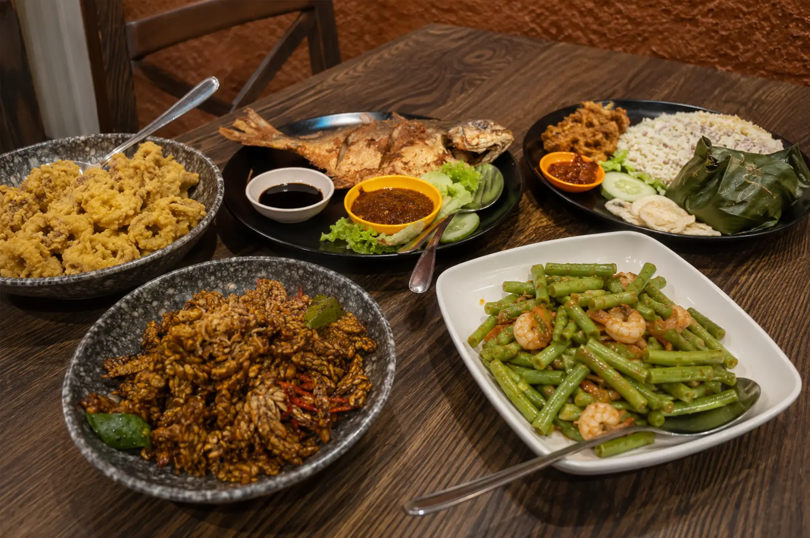 Spread of Indonesian dishes at Bara Food Tanjong Pagar, including fried seafood, grilled fish, rice, vegetables, sambal, and wrapped food.