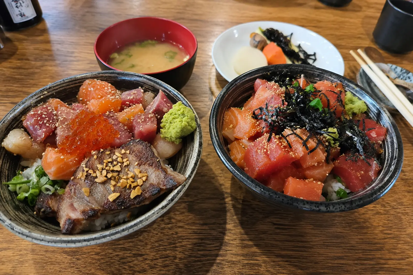 Two colorful chirashi bowls topped with assorted sashimi, served with miso soup and Japanese side dishes.
