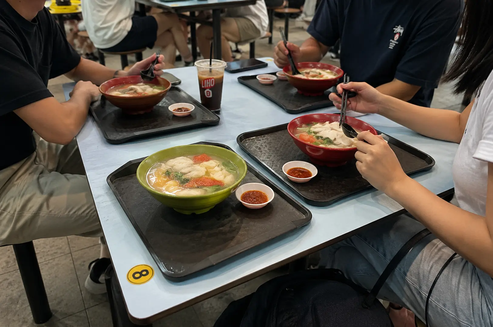 Friends enjoying hearty fish soup together at a casual Singapore food court during a relaxed meal.