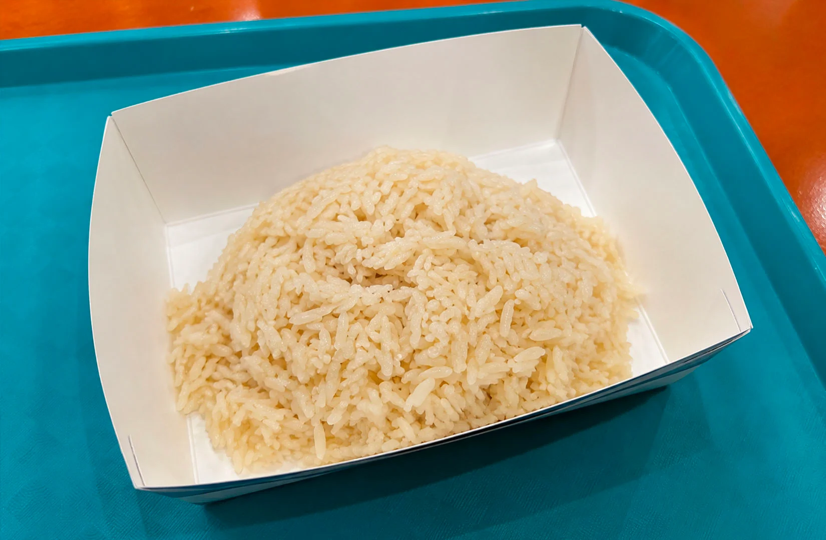 A serving of fragrant Singapore chicken rice in a takeaway paper tray, ready to be paired with poached chicken.