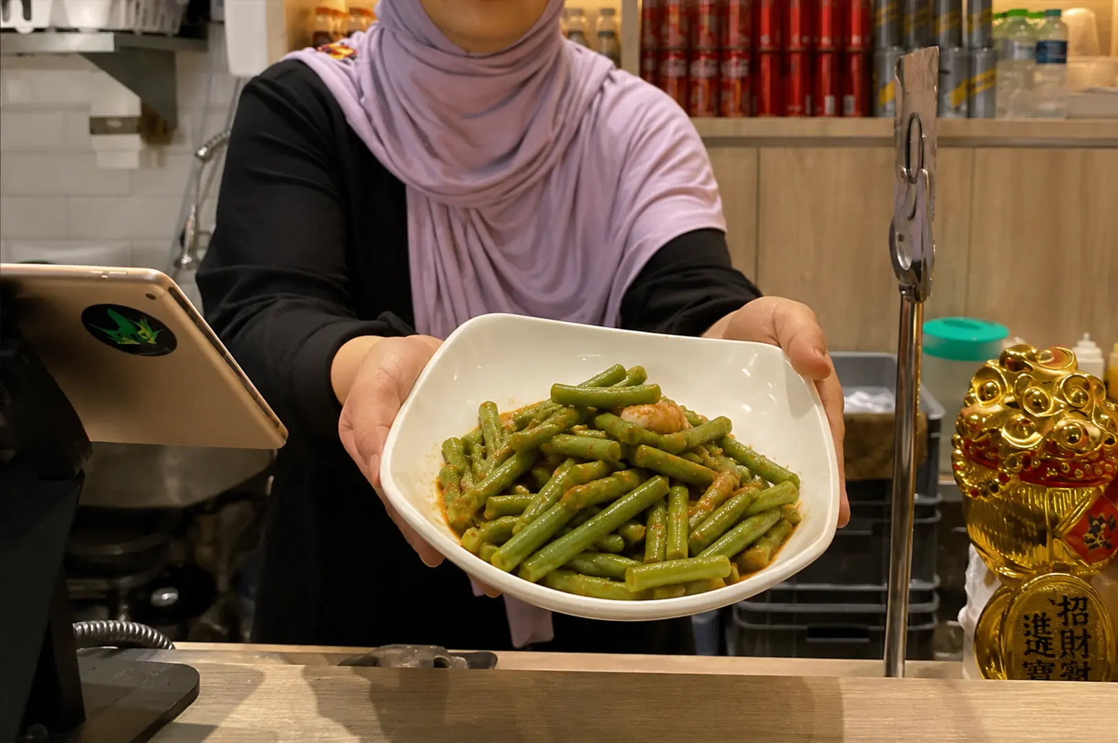 Staff member at Bara Food Tanjong Pagar presenting a bowl of green beans with prawns in a savory sauce.