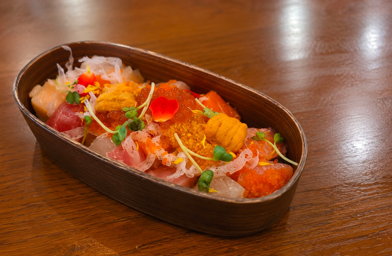 Premium chirashi sushi in a wooden box with sea urchin and salmon roe.
