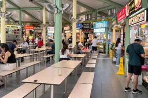 A busy view of Adam Road Food Centre with rows of food stalls, dining tables, and diners.