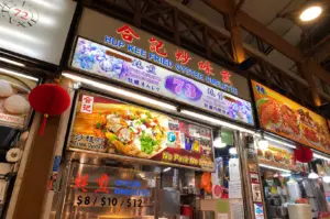 Hup Kee Fried Oyster Omelette stall at a bustling Singapore food centre, with its large illuminated sign and traditional Chinese décor