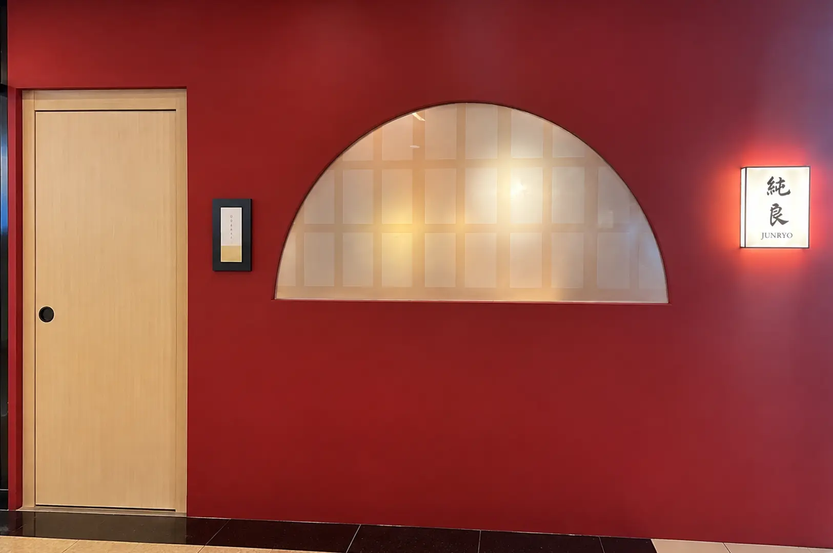 Red restaurant entrance with a light wood door, arched frosted window, and illuminated Junryo sign.