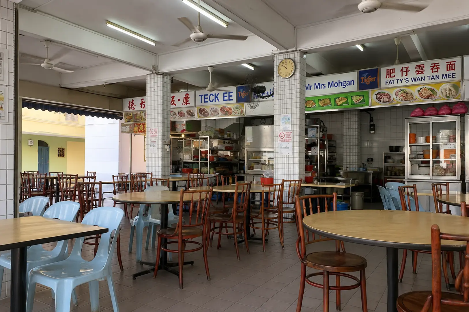 Spacious local food court with multiple hawker stalls, ceiling fans, and casual dining tables.
