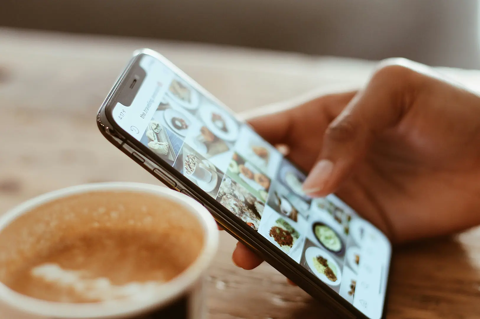 A person browses food options on a smartphone while sitting at a table with a drink.