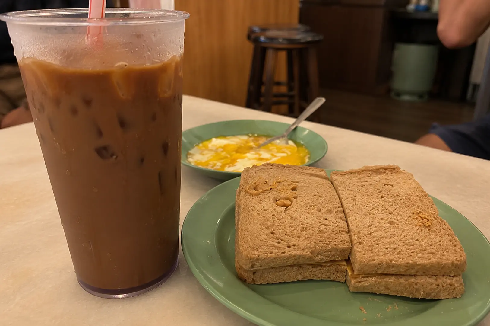 Traditional Singapore kaya toast breakfast with iced kopi, soft-boiled eggs, and kaya toast at a kopitiam.