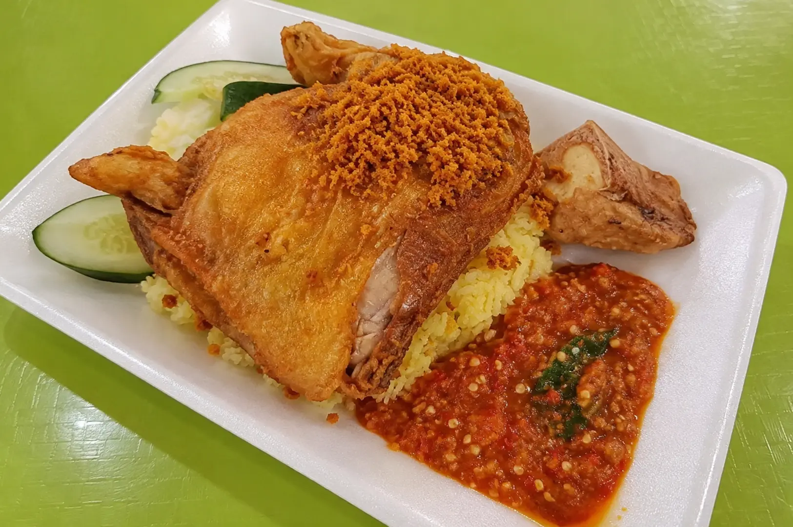 A serving of ayam penyet with crispy fried chicken, fragrant rice, cucumber, and spicy sambal.