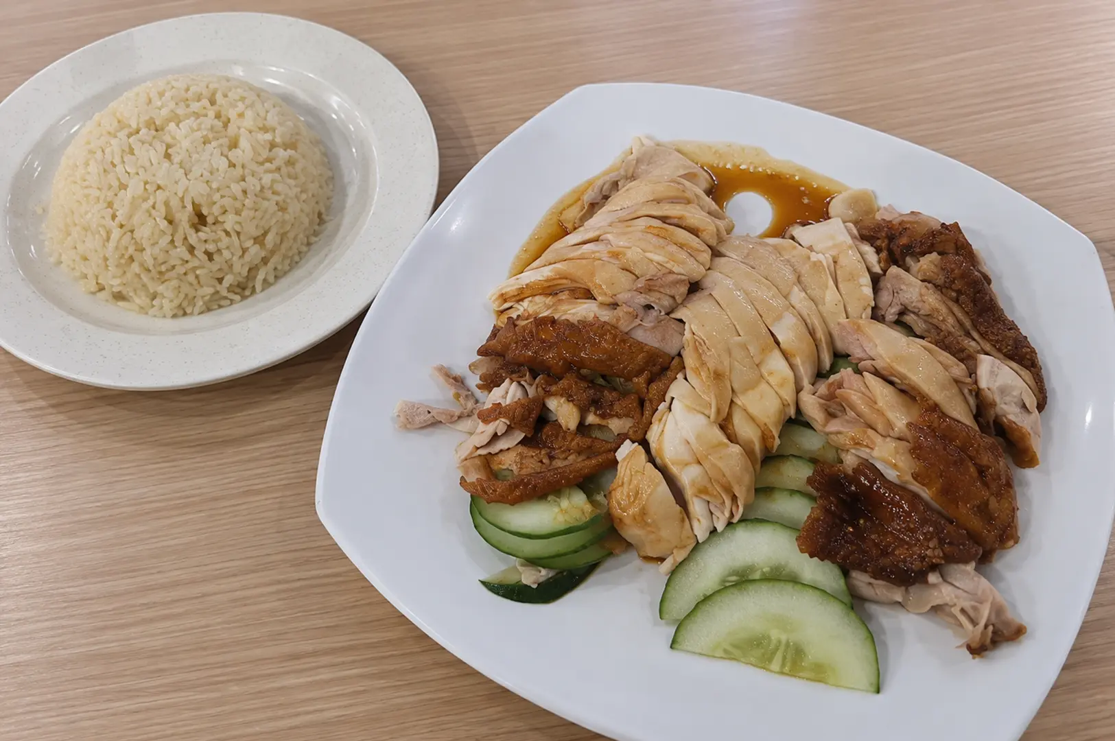 A plate of sliced chicken served with fragrant rice, cucumber, and savory sauce.