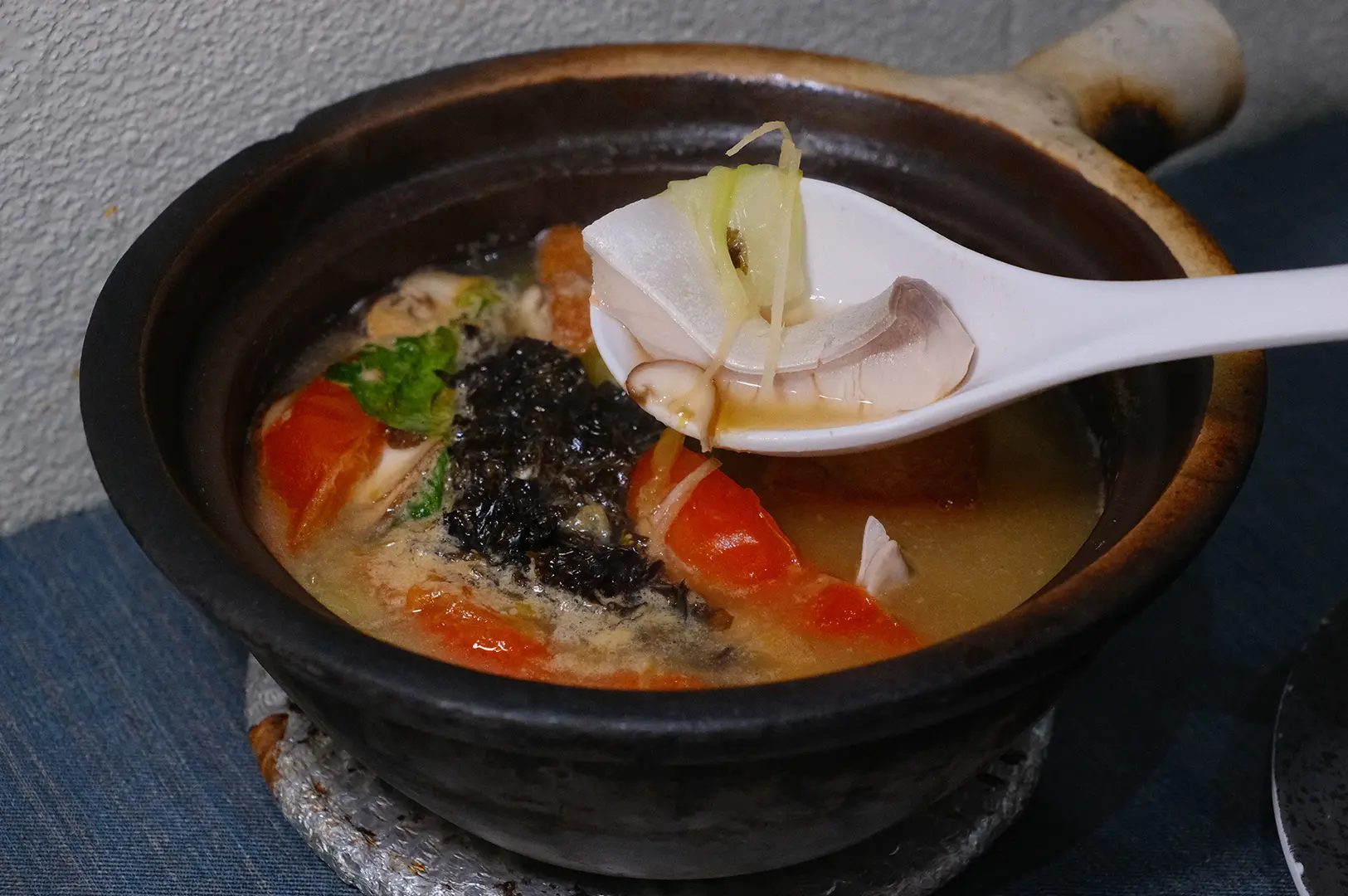 A bowl of Grandpa’s Pomfret Soup served in a clay pot with fish, vegetables, and herbs.