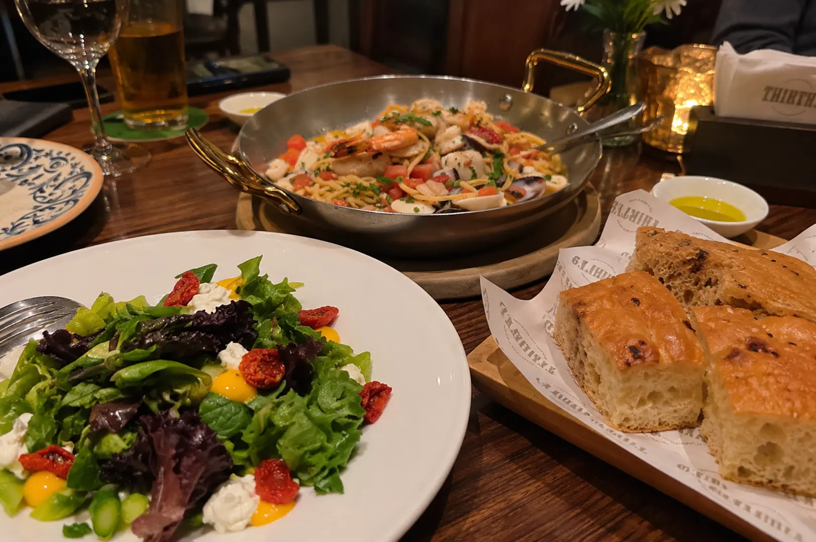 Italian dining table with seafood pasta, fresh salad, focaccia bread, and drinks.