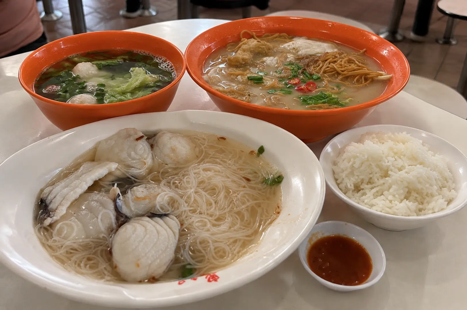 Teochew fish porridge meal with fish balls, noodles, soup, rice, and dipping sauce on a table.