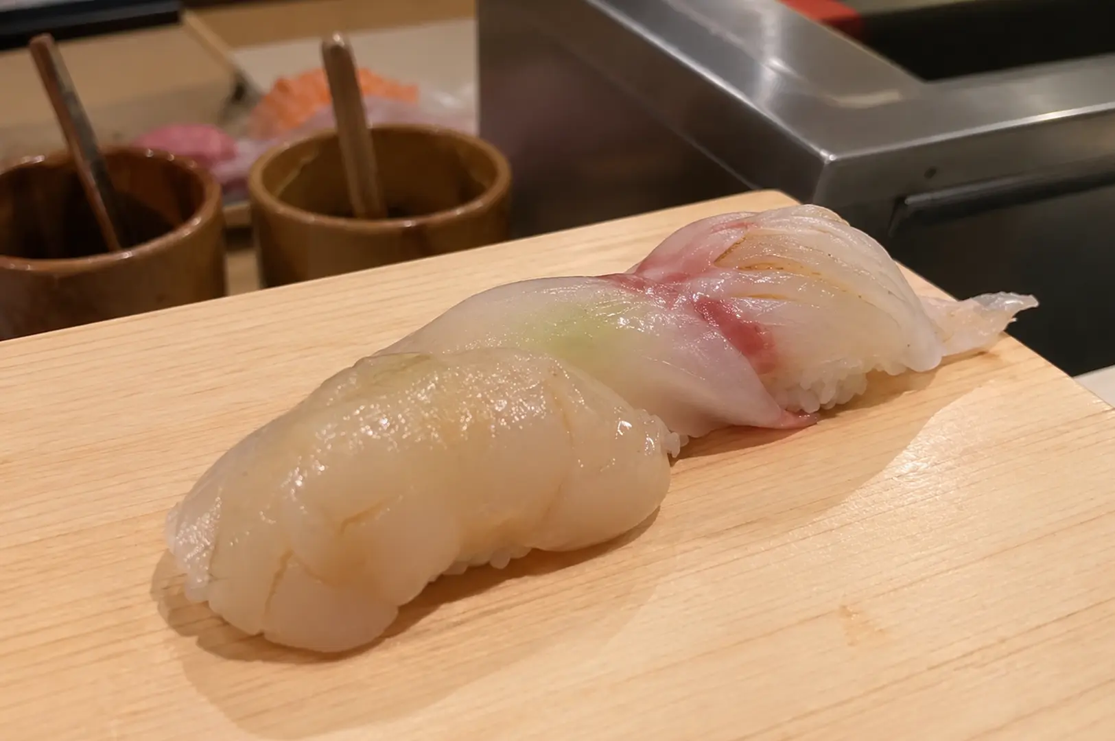 Three pieces of fresh white-fish nigiri sushi arranged on a light wooden counter.