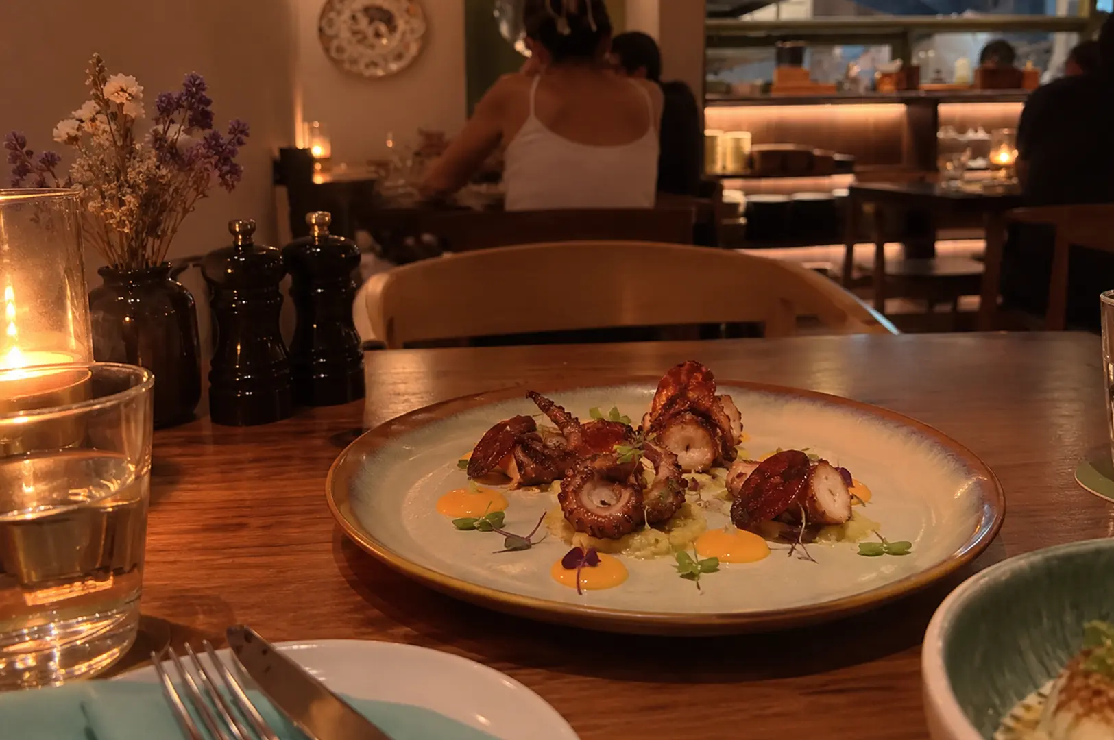 Grilled octopus elegantly plated with sauce and microgreens in a warmly lit restaurant.