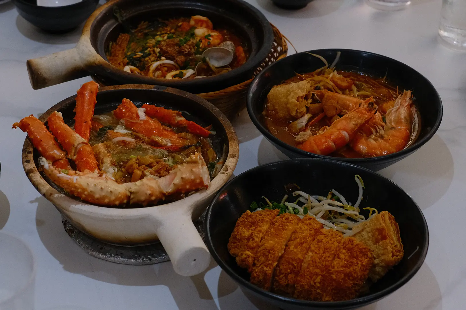 A spread of seafood dishes featuring king crab, prawns, noodles, and crispy sides.
