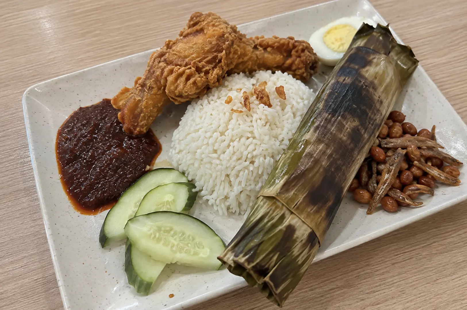 A plate of Royal Rumble nasi lemak with fragrant rice, fried chicken, egg, sambal, peanuts, anchovies, and cucumber.